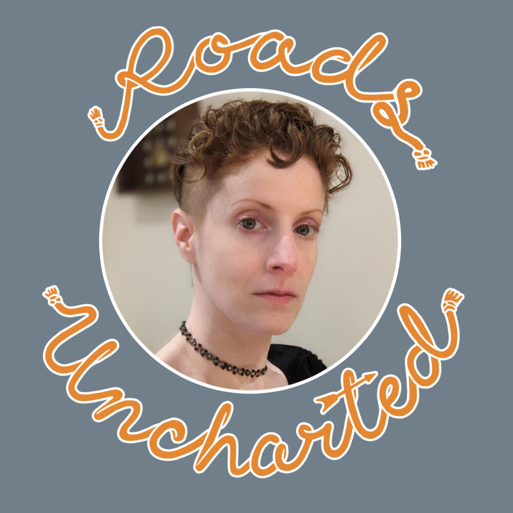 A headshot of Dax. A White woman with short, curly red hair with close cropped sides and green eyes, she wears a black shirt and matching choker. Image is framed in a white circle with orange "Roads Uncharted" surrounding it.