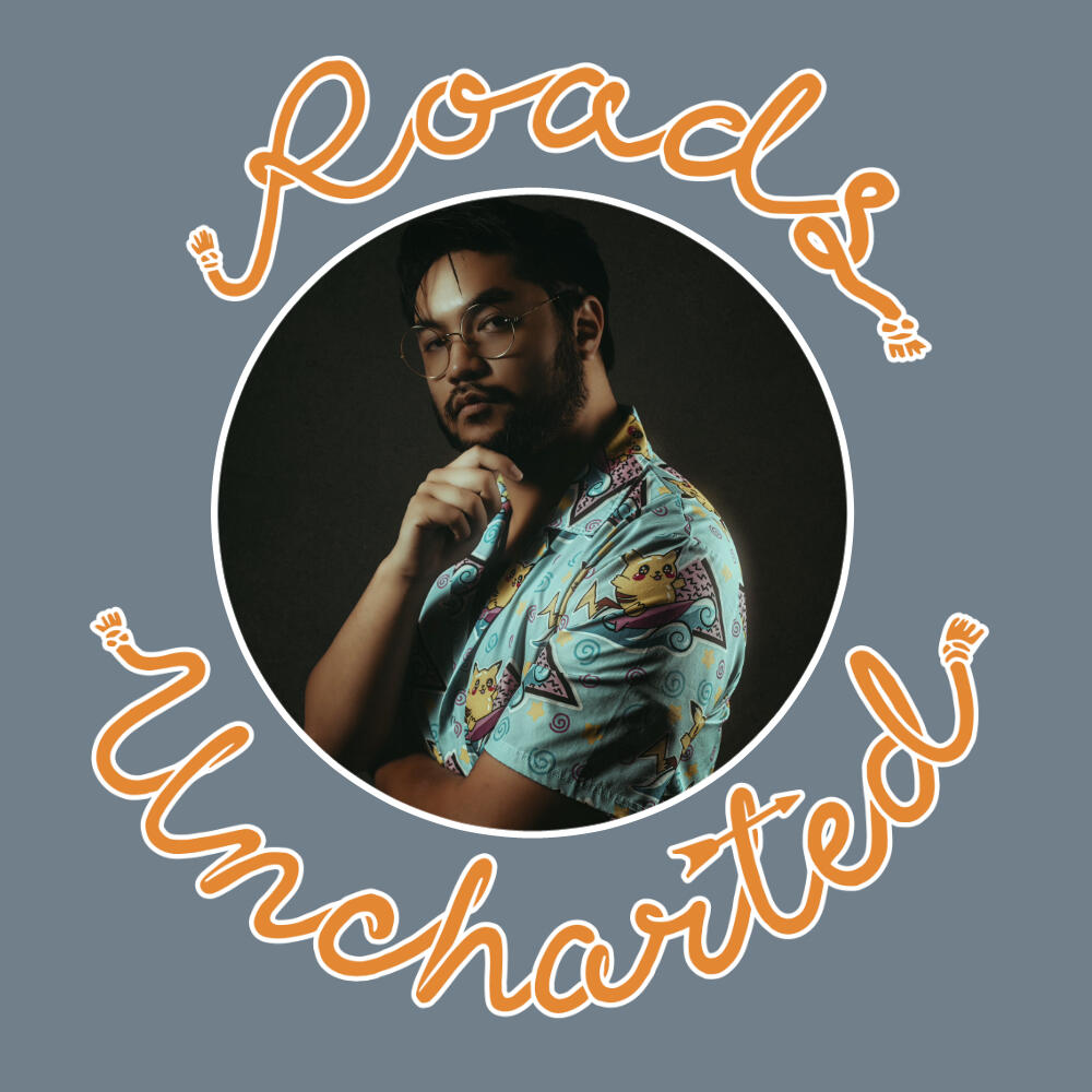 A headshot of Kappa. Bearded Asian man with wire rim glasses, dressed in a Hawaiian style shirt with a Pikachu design. Image is framed in a white circle with orange "Roads Uncharted" surrounding it.